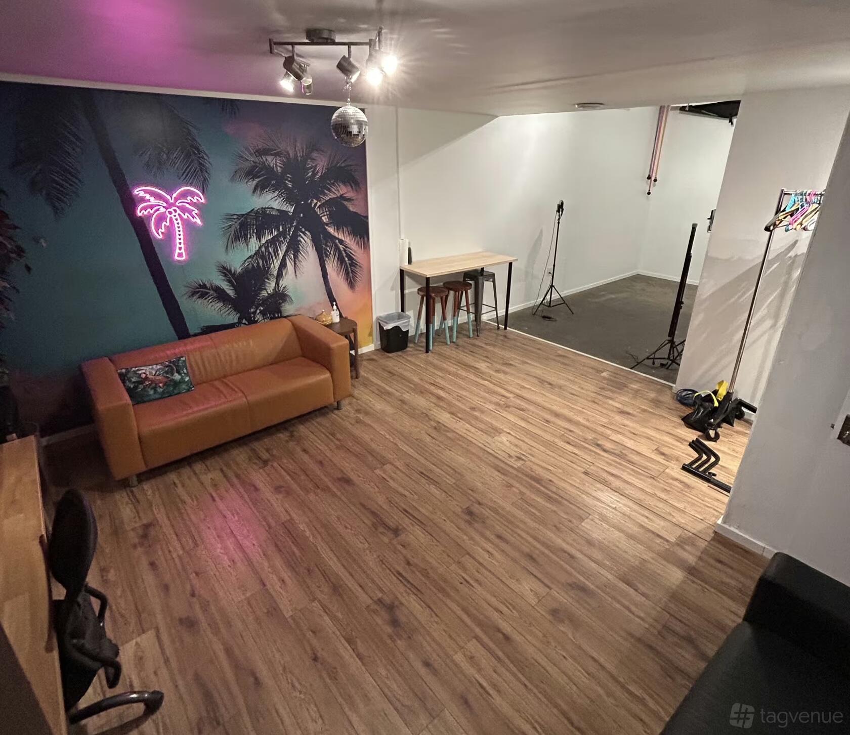 A creative space with a neon palm tree mural, leather sofa, wood floors, and photo equipment at Palm Street Studios.