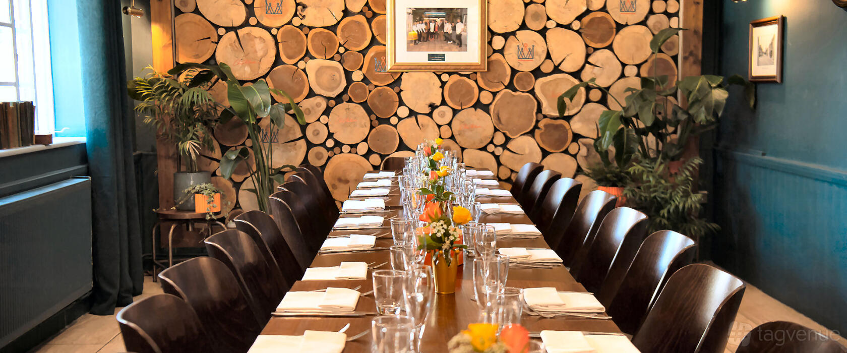A restaurant with a long wooden table set for dining, surrounded by dark chairs and a log wall at The Crown Inn at Burnham Beeches.