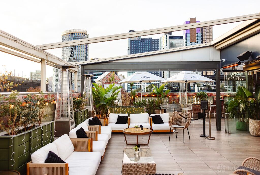 A rooftop bar with white cushioned sofas, potted plants, and city skyline views at Mirror Mirror Rooftop Lounge.