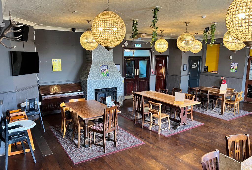 An event space in a pub with large globe pendant lights, wooden tables, and a decorative fireplace at The Glasshouse.