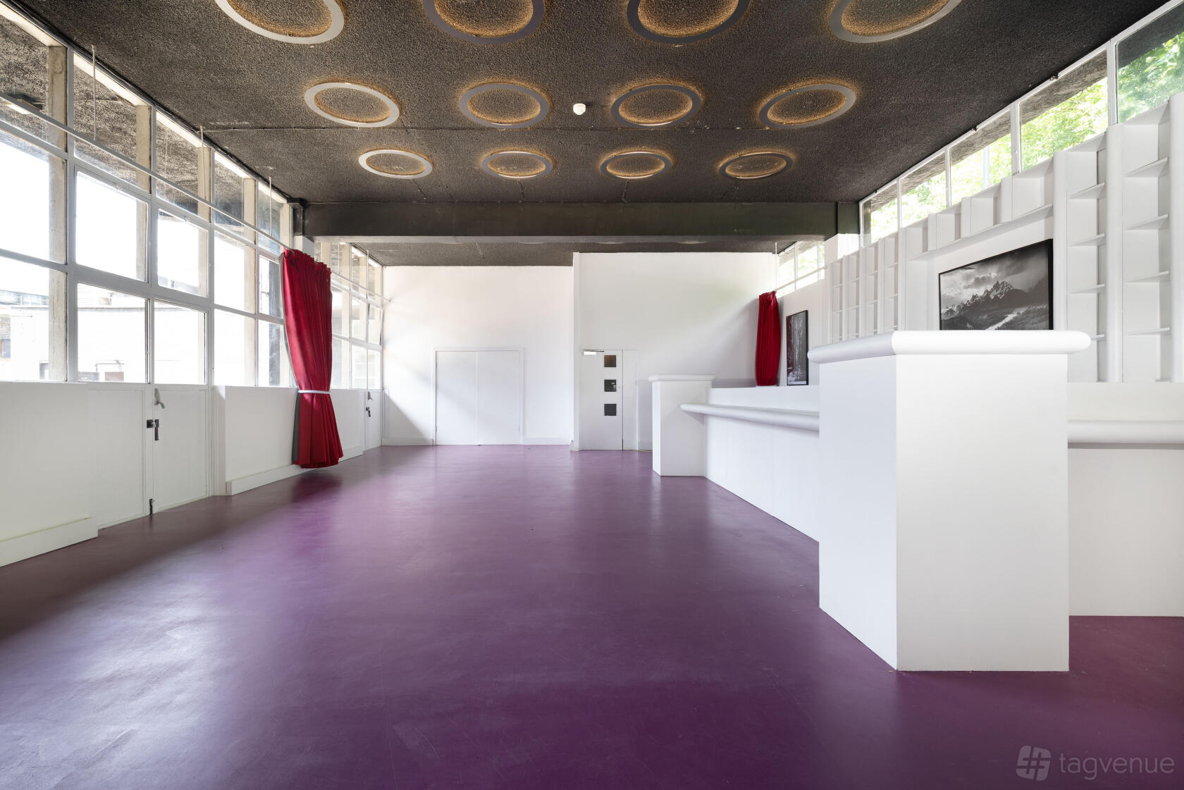 An event space with purple flooring, large windows, red curtains, and a long white bar at Proposition Studios.