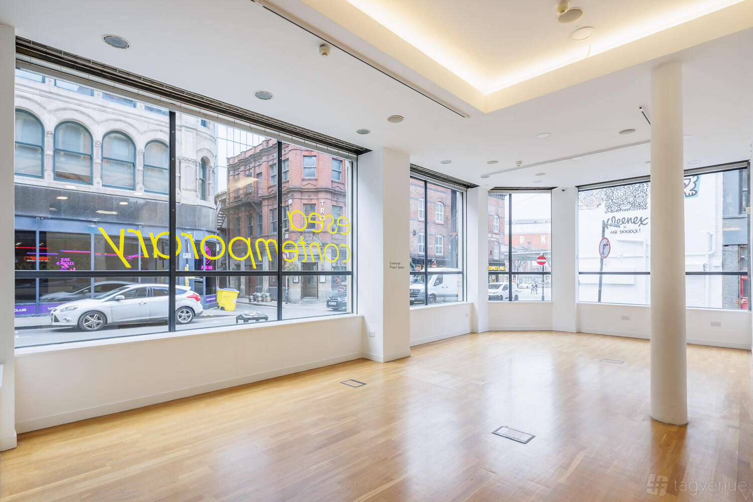 A gallery space with floor-to-ceiling windows, light wood flooring, and recessed ceiling lights at esea contemporary.