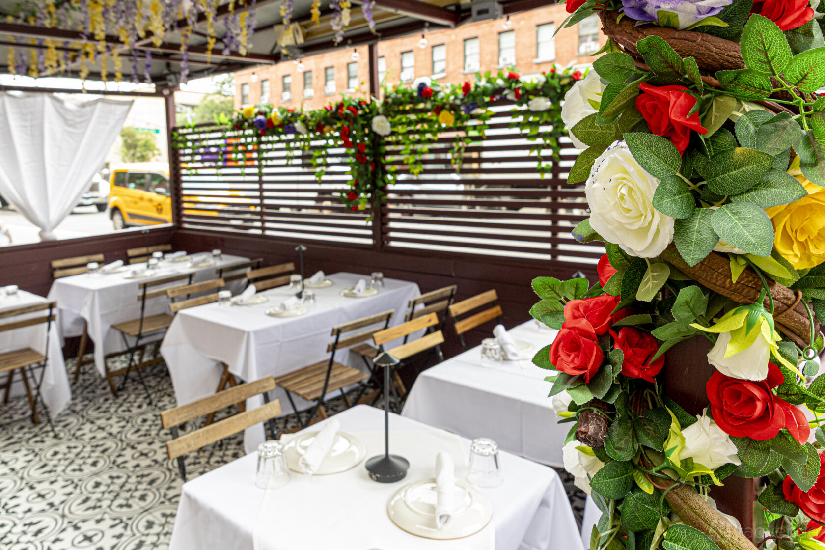 An outdoor restaurant space with floral garlands, patterned tile floor, and tables draped in white linens at Balade.
