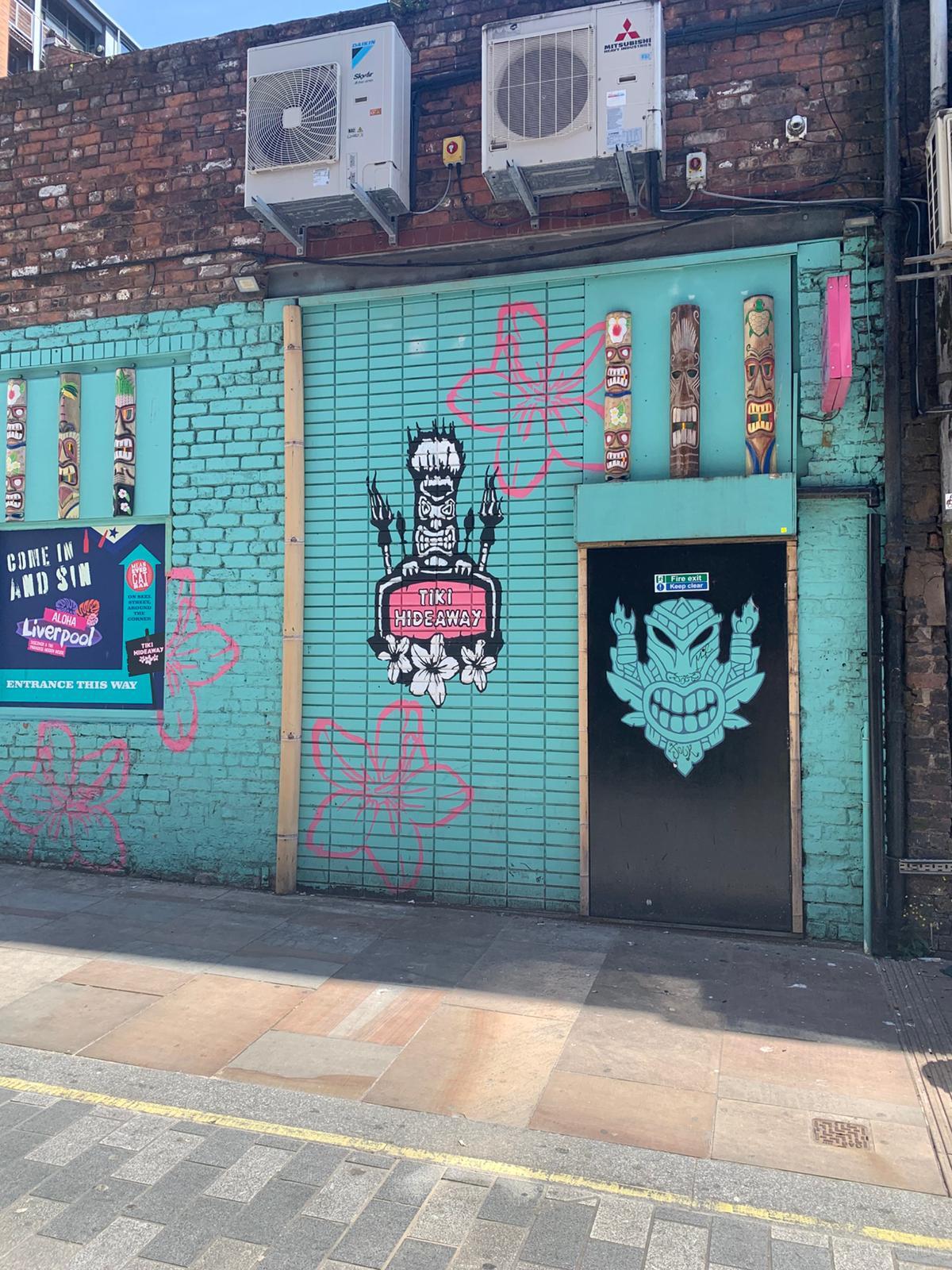 A versatile event space with turquoise brick walls, tiki murals, and pink floral graffiti at Tiki Hideaway Liverpool.