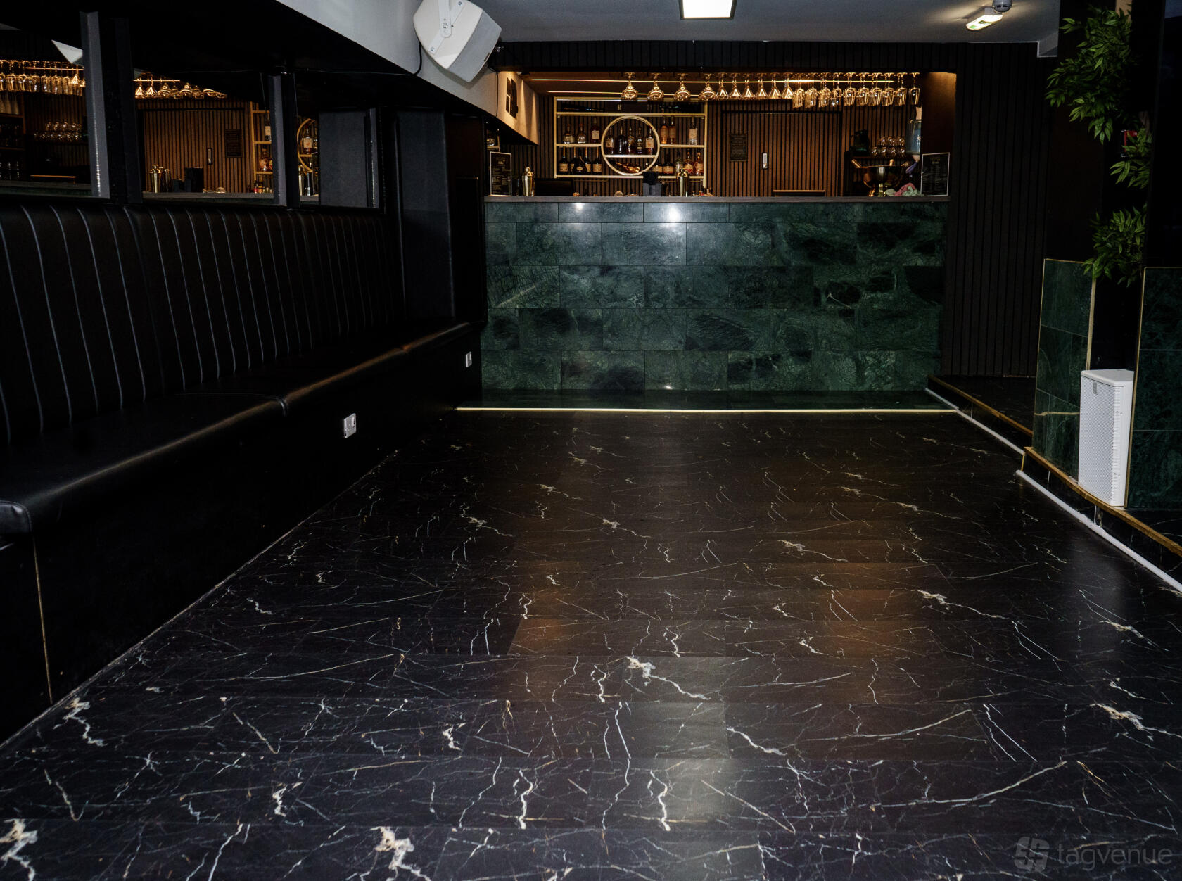 A bar with marble flooring, dark banquette seating, and a green marble bar counter at Basement 144.