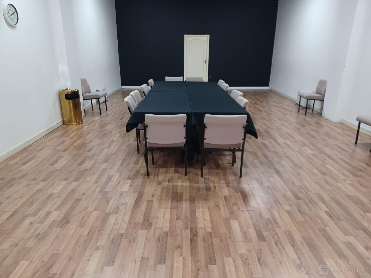 A meeting room with wood flooring, neutral chairs, and a central rectangular table with a black tablecloth at Glasgow Rooms.