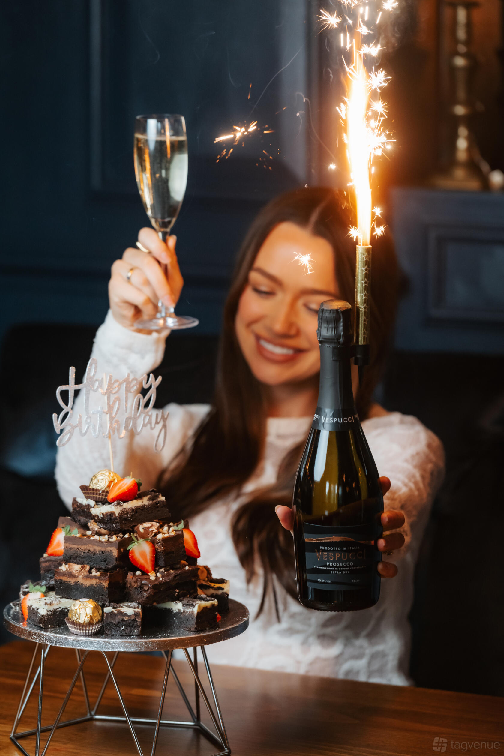 A function room with a guest holding a birthday cake and a bottle of sparkling wine with a sparkler at Manahatta Deansgate.