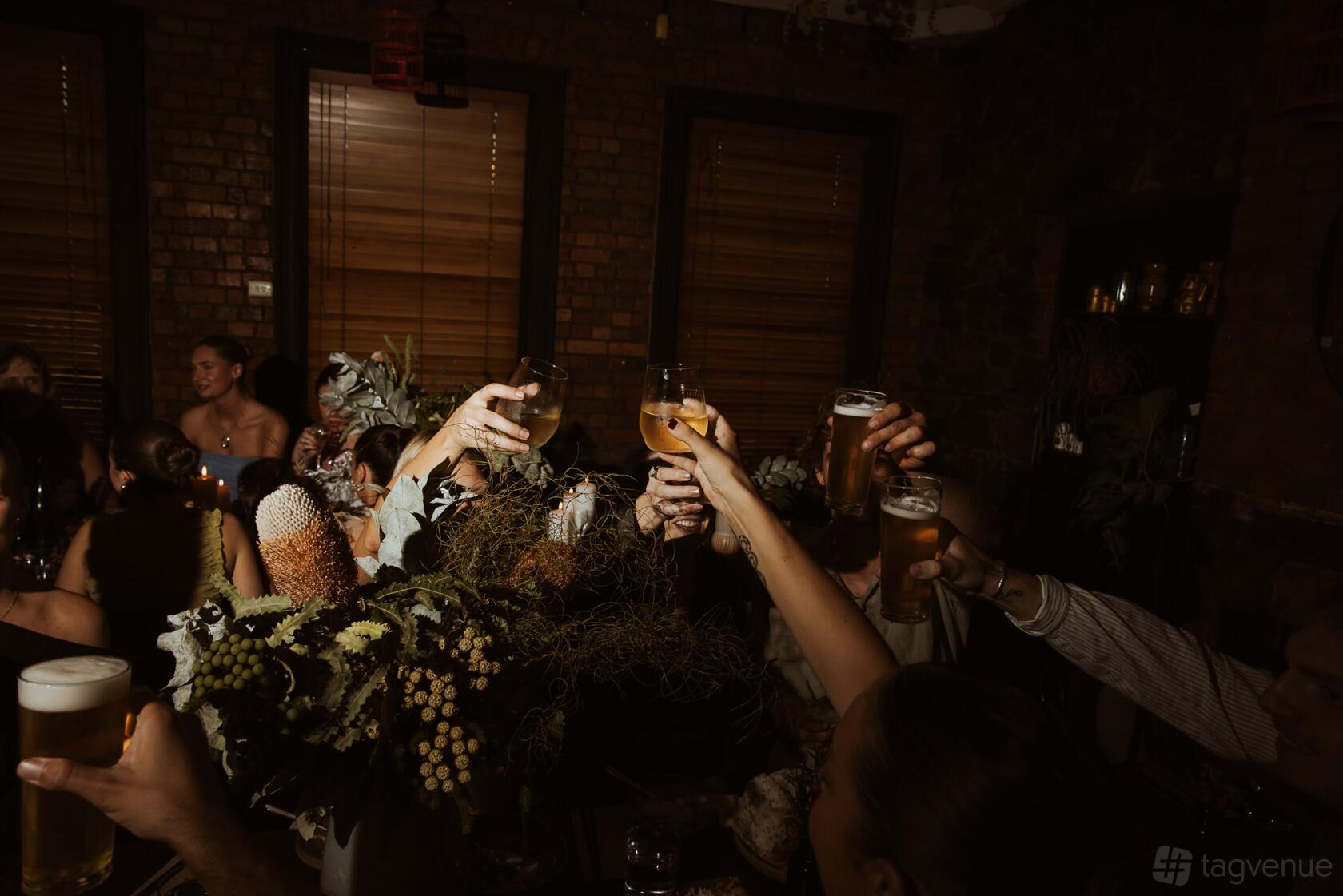 A function room in a restaurant with exposed brick walls, wooden blinds, and guests raising drinks at Rice Paper Scissors Fitzroy.