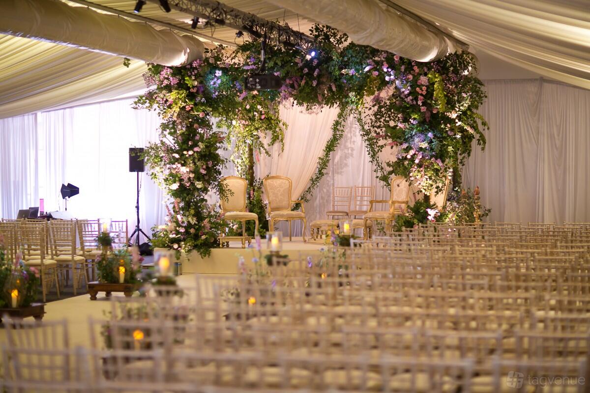 An event space with rows of light wooden chairs and a floral-decorated stage under draped white fabric at Tewinbury Farm Hotel.