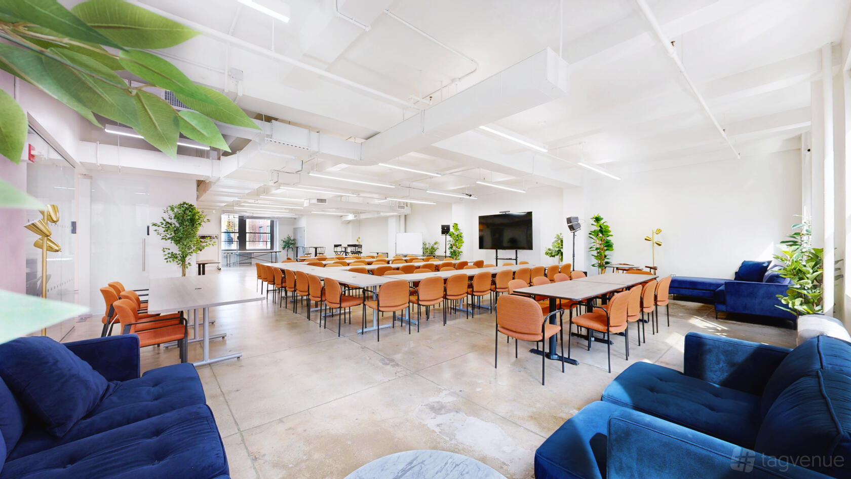 A meeting centre with rows of orange chairs, long tables, large windows, and a presentation screen at Event Loft 1505.