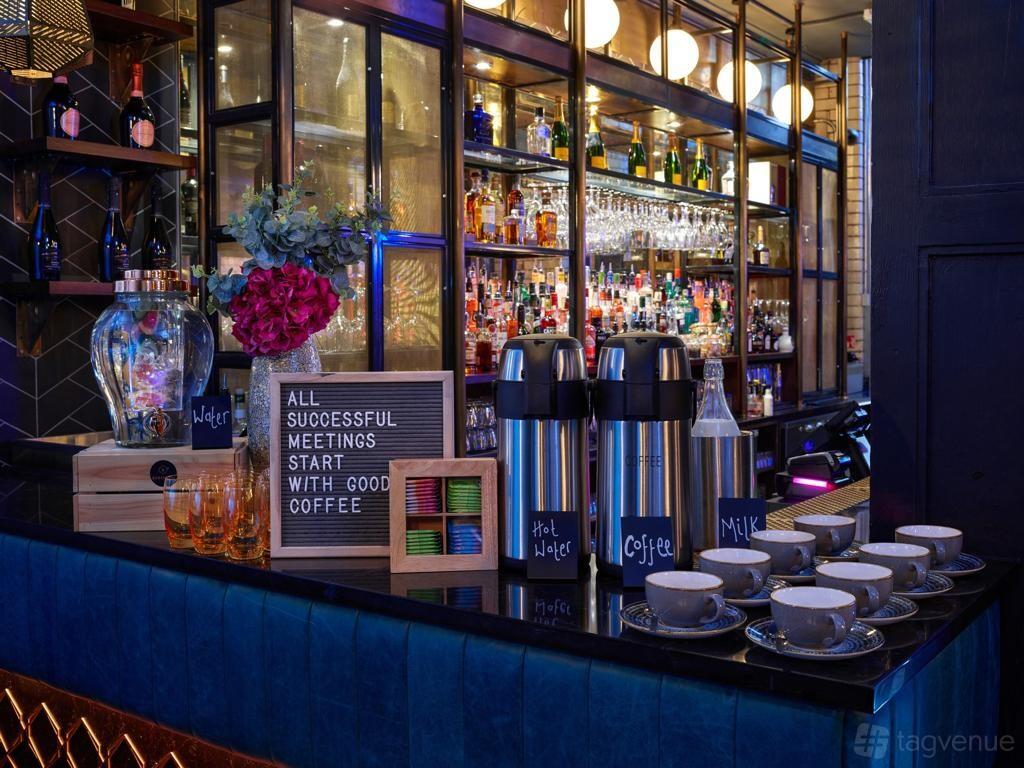 A cocktail bar with a mirrored back bar, glassware, and a coffee station on the counter at Manahatta Greek Street.