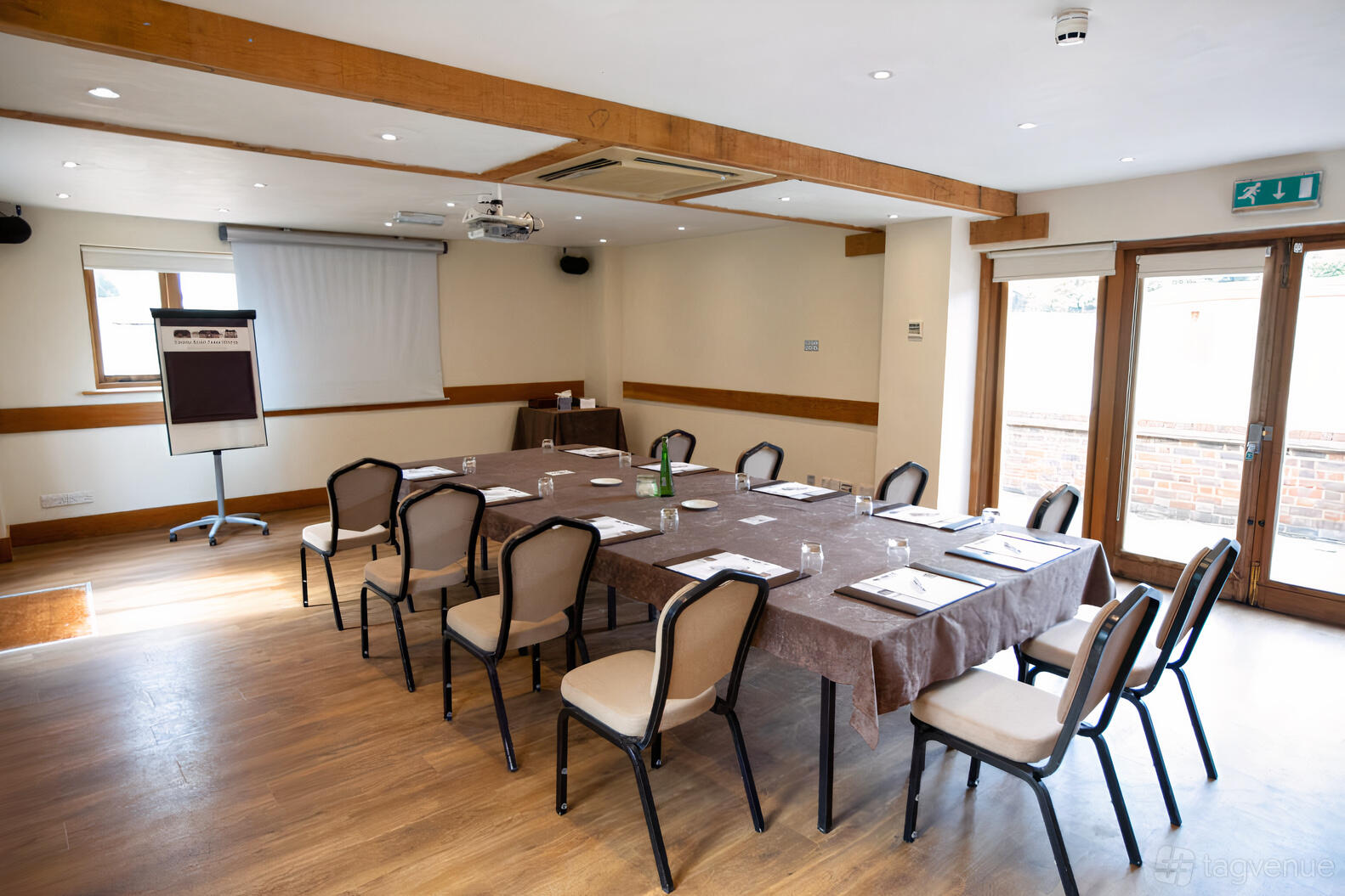 A meeting room with a U-shaped table setup, brown linens, flip chart, and projector at Tewinbury Farm Hotel.