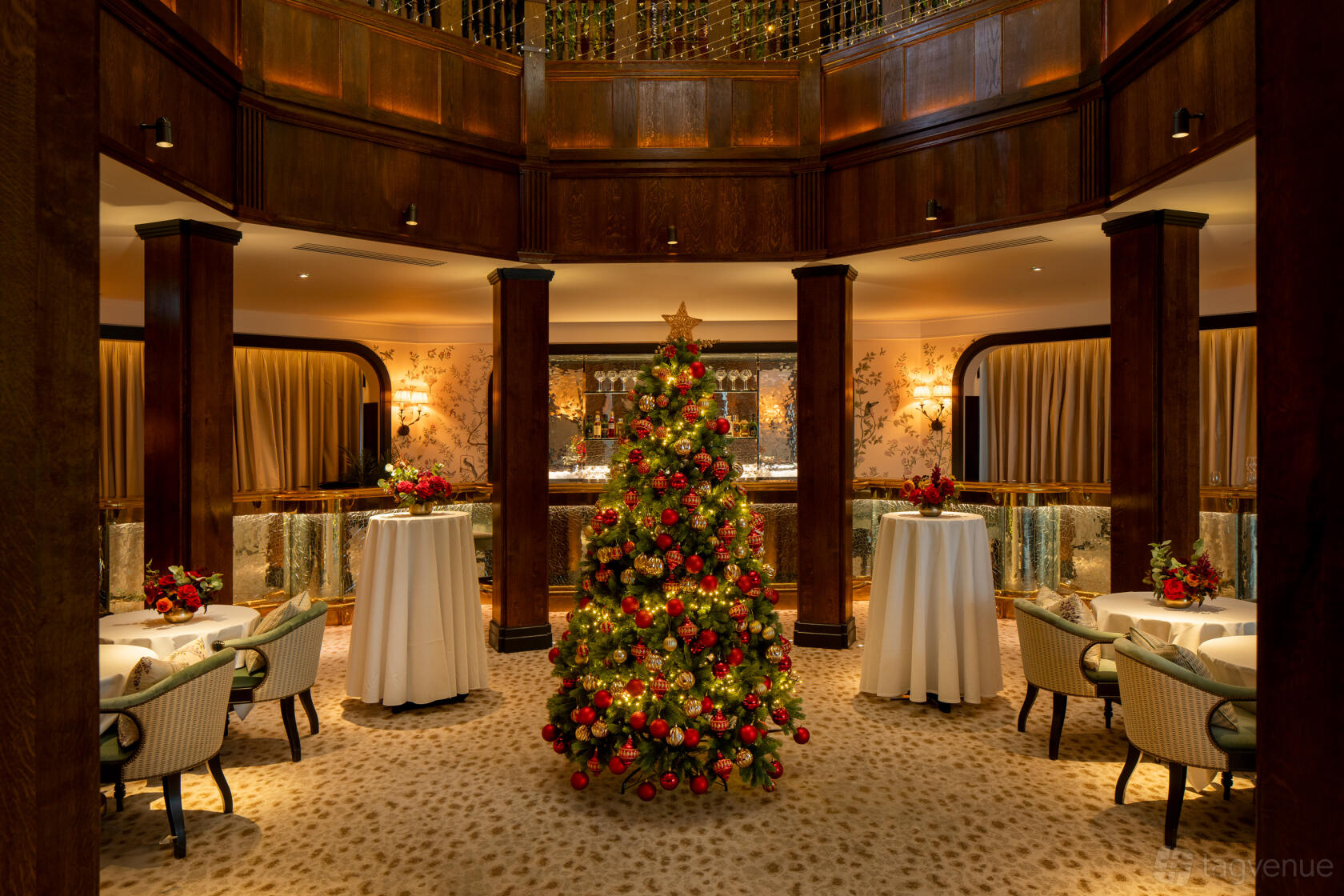 An event space with a decorated Christmas tree, round tables with white linens, and wood-paneled walls at L'oscar London.