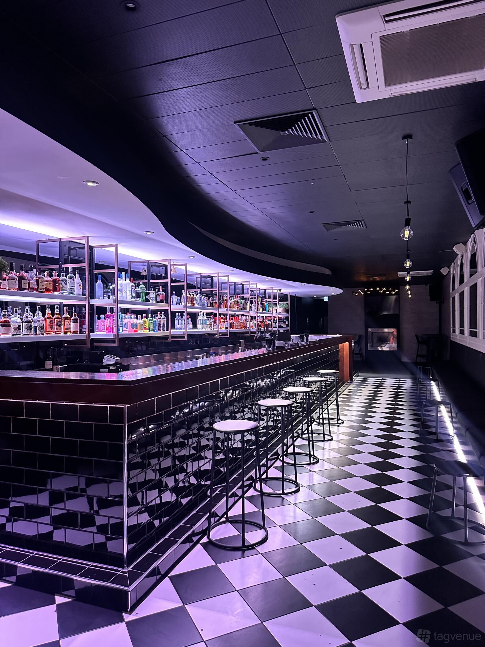 A lounge with a long mirrored bar, black-and-white checkered floors, and backlit shelving at Amani Bar.