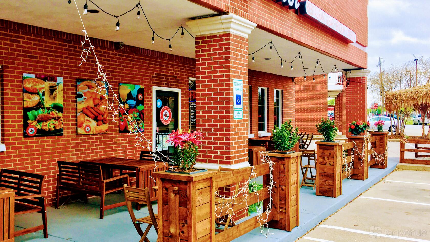 An outdoor restaurant patio with brick columns, string lights, wooden tables, and potted plants at Spicy Zest Cafe & Boba.