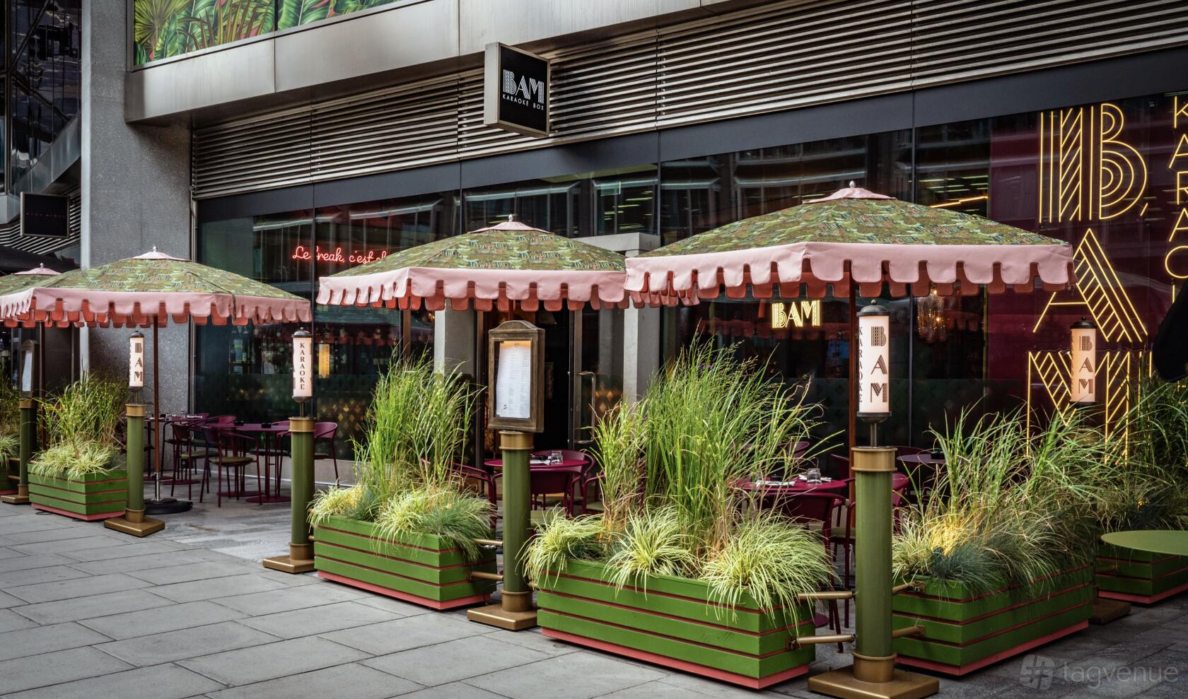 An outdoor terrace at BAM Karaoke Box with large umbrellas, planter boxes with tall grass, and bistro tables.