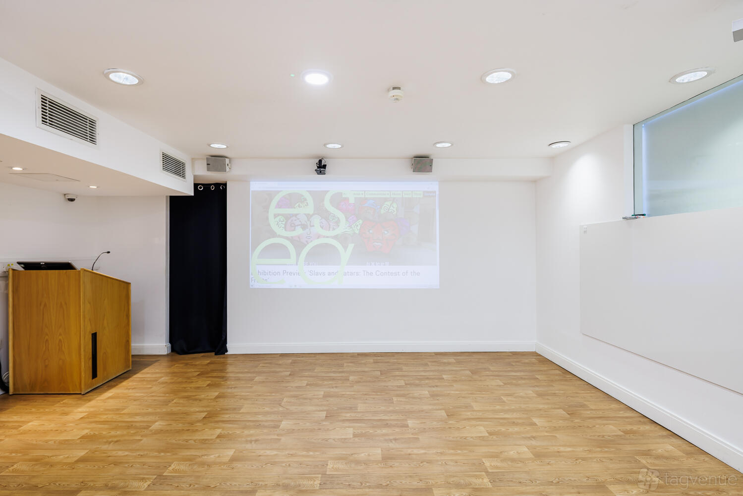 A gallery function room with a wood floor, projector screen, lectern, recessed lighting, and large window at esea contemporary.