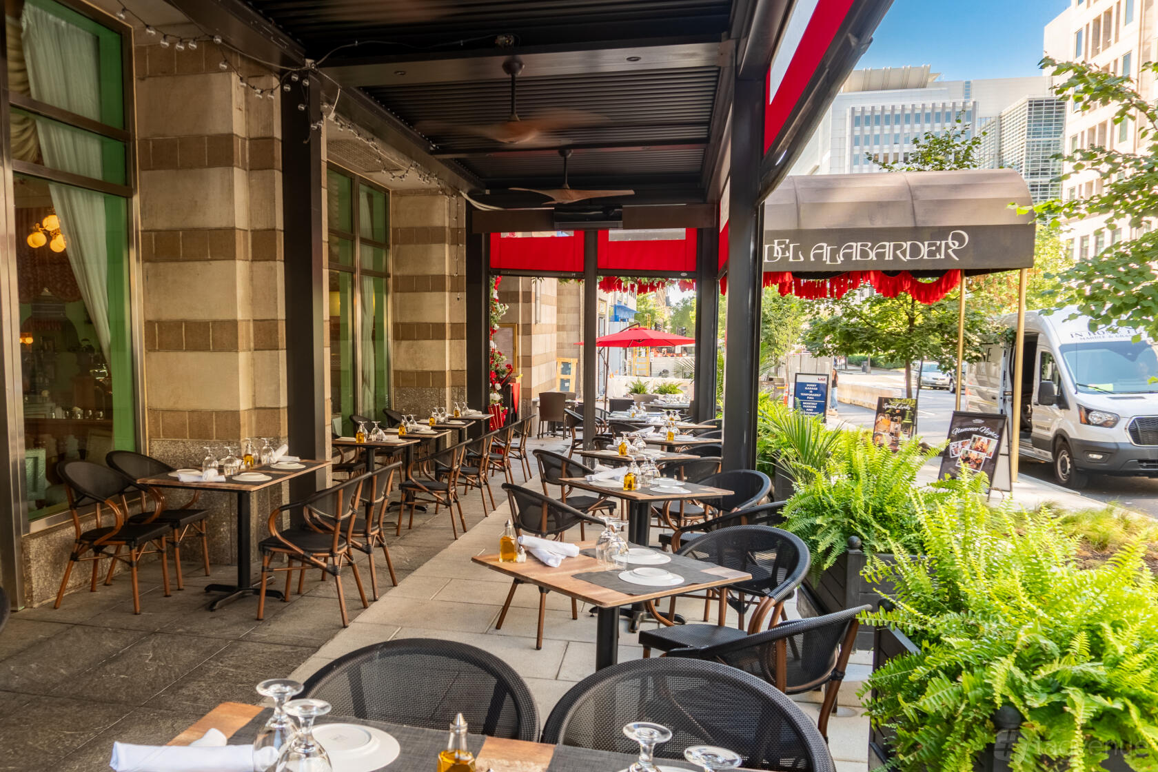 An outdoor restaurant patio with black chairs, wood tables, and potted ferns at Taberna Del Alabardero.