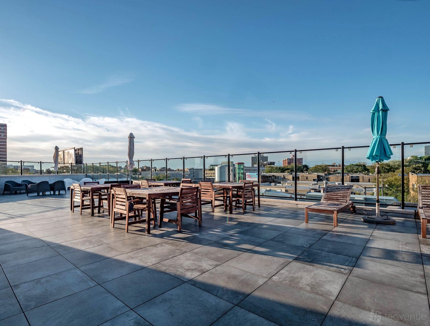 A rooftop space with wooden tables, chairs, glass railing, and city views at DeskLabs.