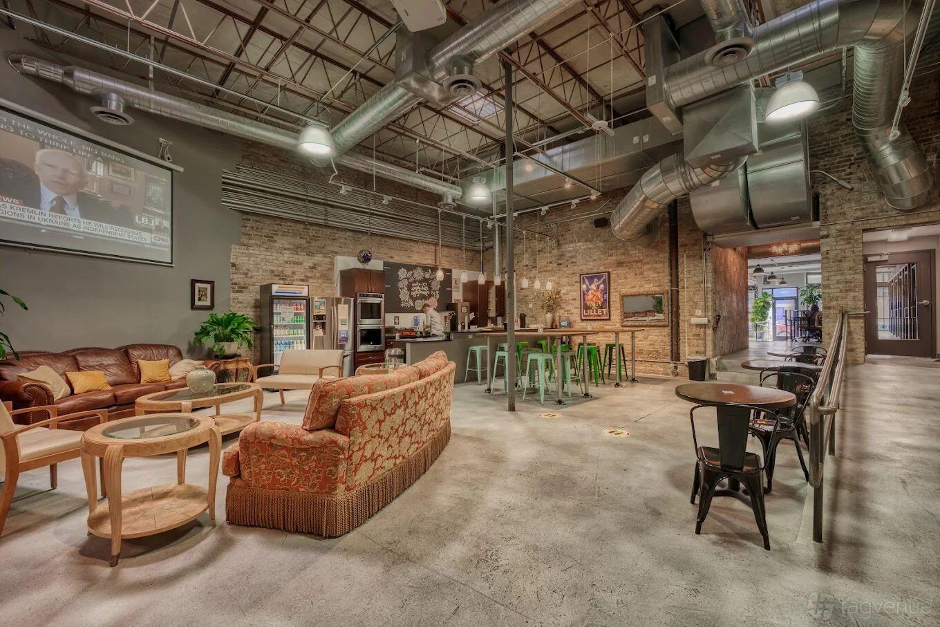 An open event space with exposed brick walls, industrial ceilings, eclectic lounge seating, and a kitchenette at DeskLabs.