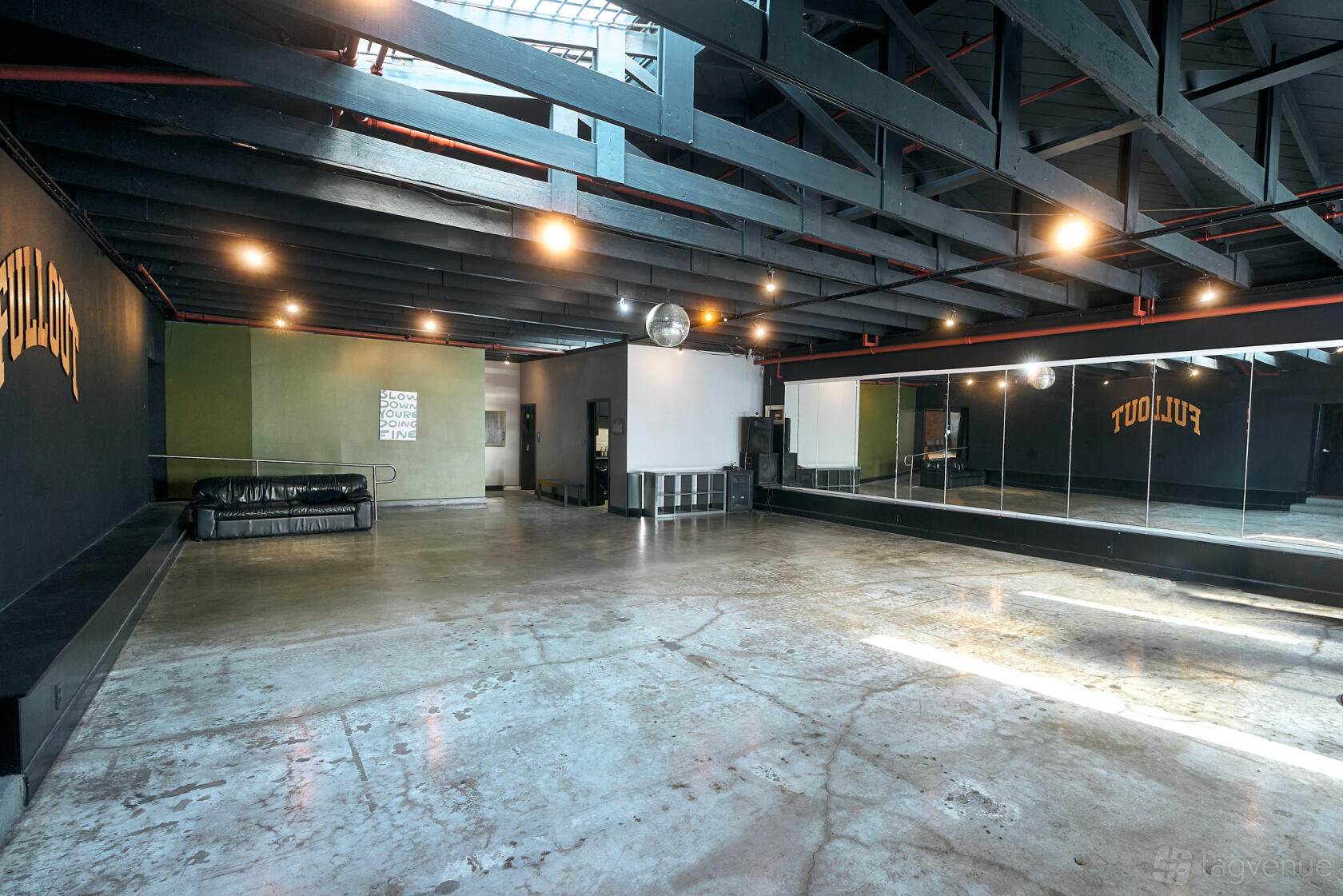 A dance studio with polished concrete floors, wall-length mirrors, and exposed beams at Full Out Studios.