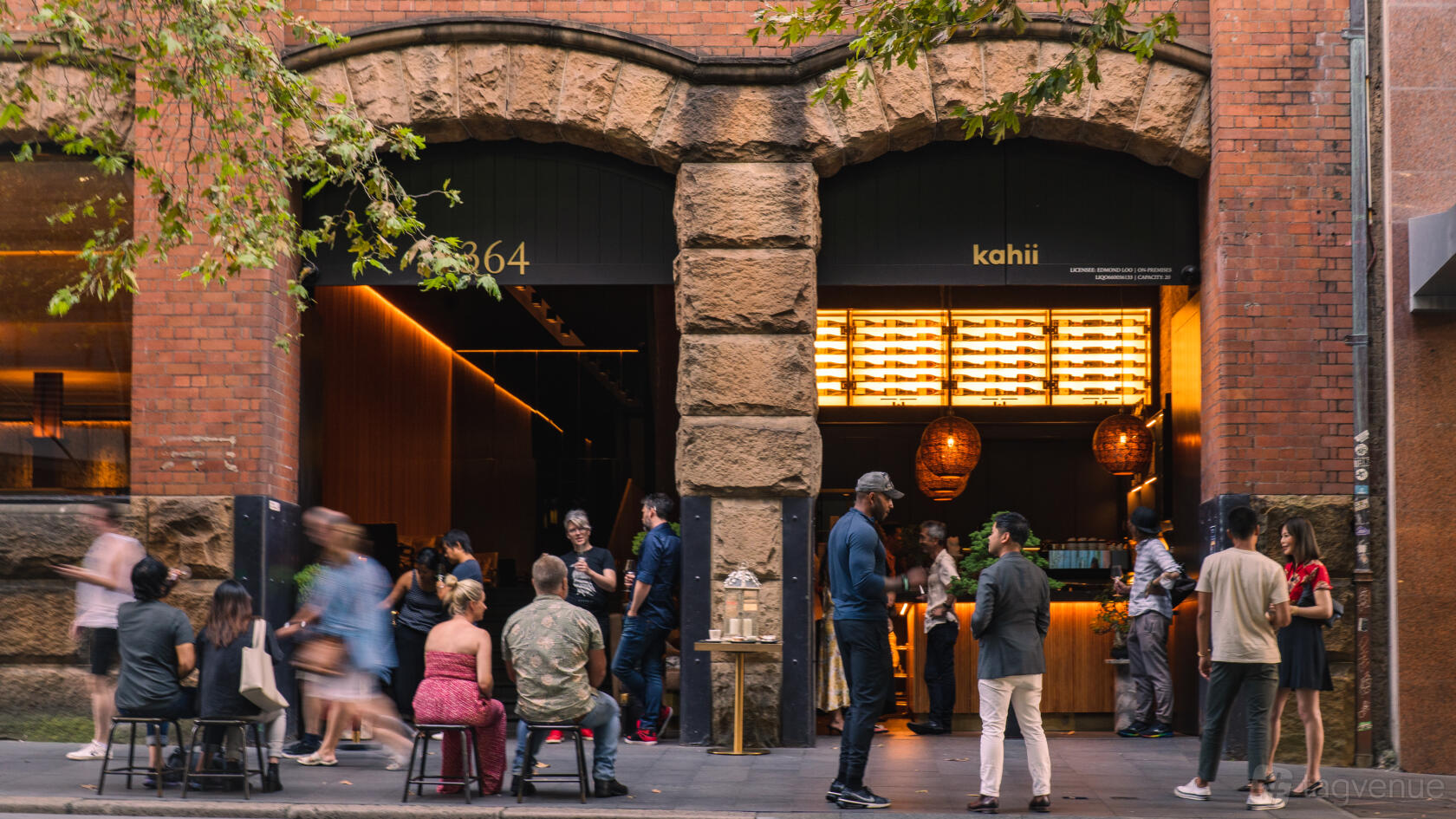 A bar with open archways, exposed brick facade, and patrons seated outdoors at KAHII | Kissaten & Wine Bar.