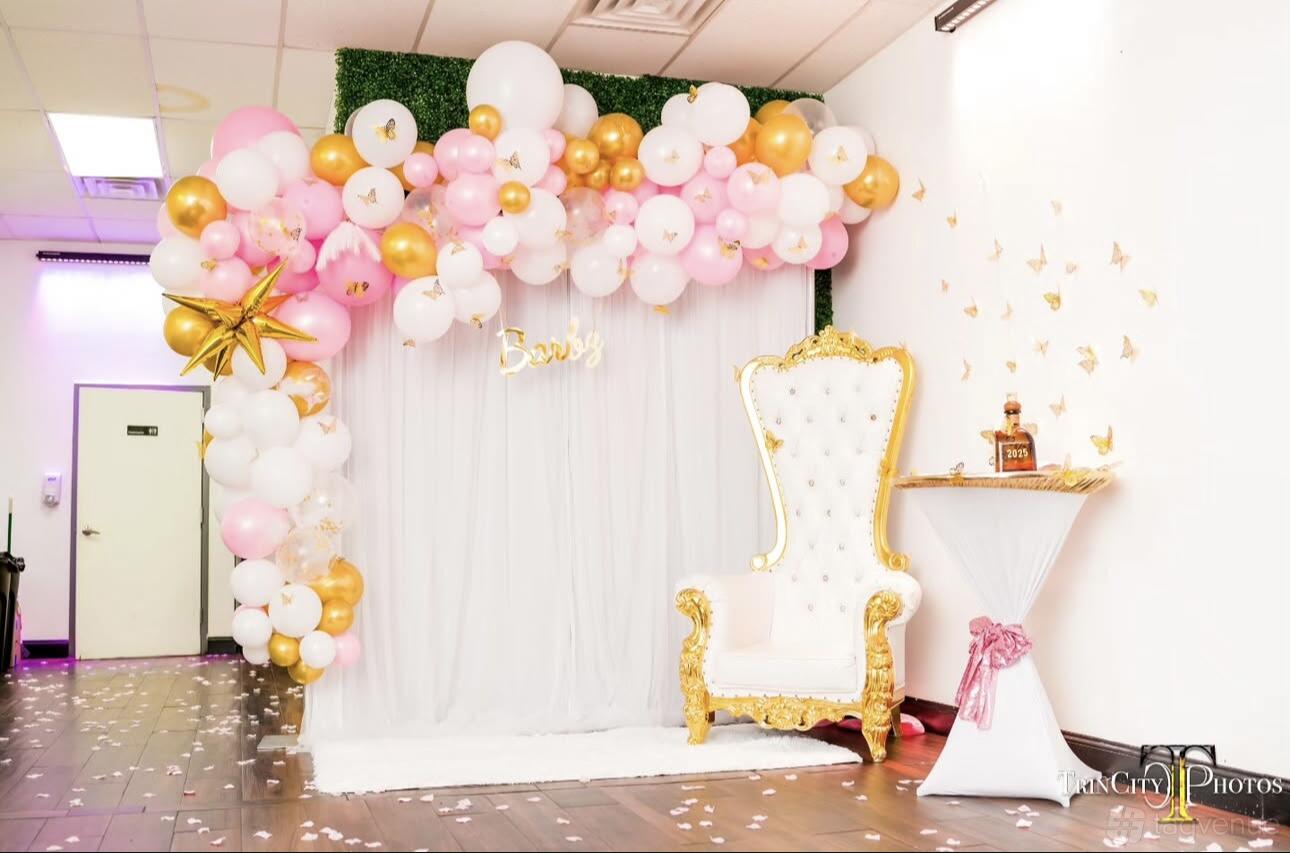 An event venue with a balloon garland backdrop, gold-trimmed white chair, and cocktail table at Parkway Studios.