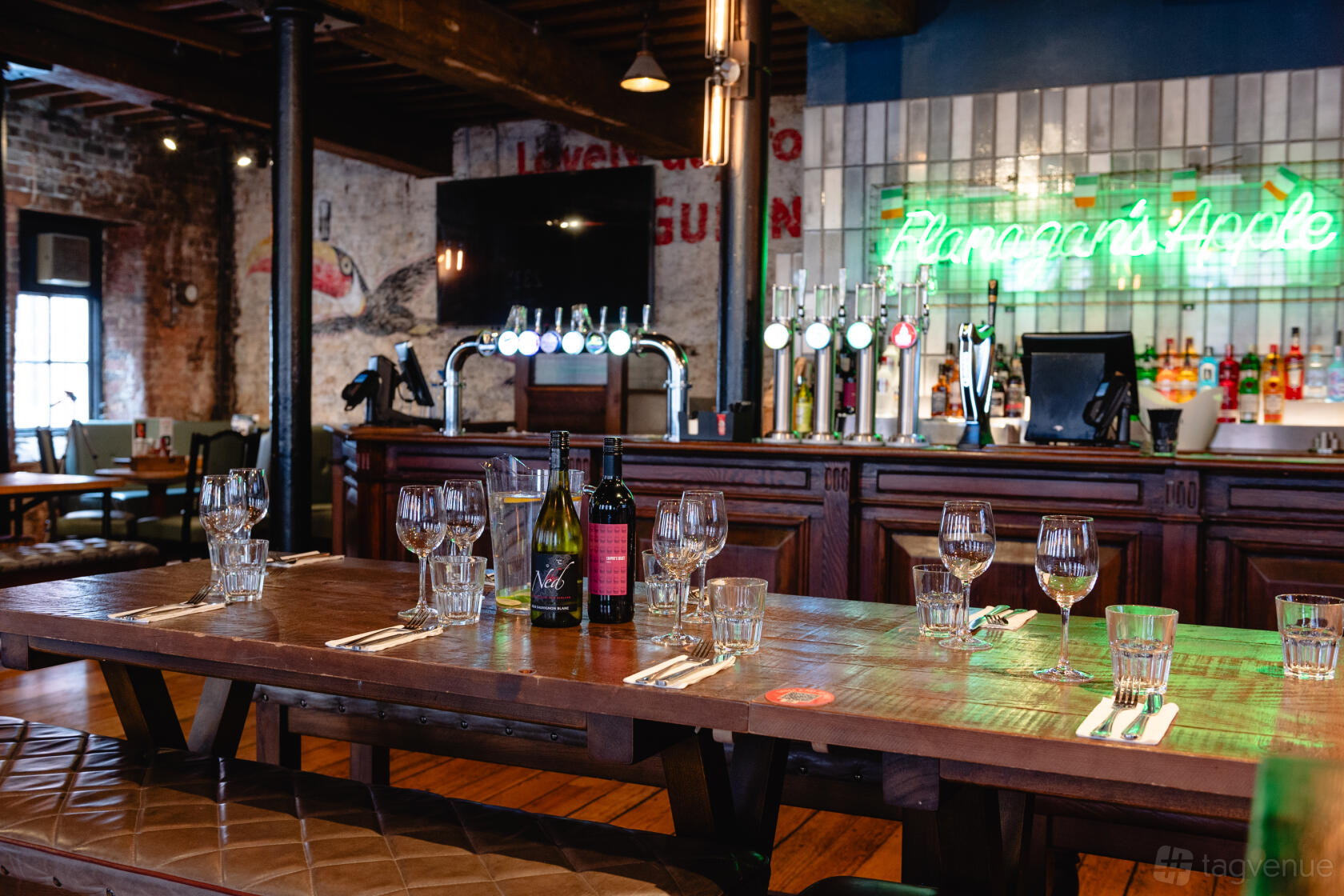 An event space in a pub with a wooden table set for dining, exposed brick walls, and a neon sign at The Flanagan's Apple.