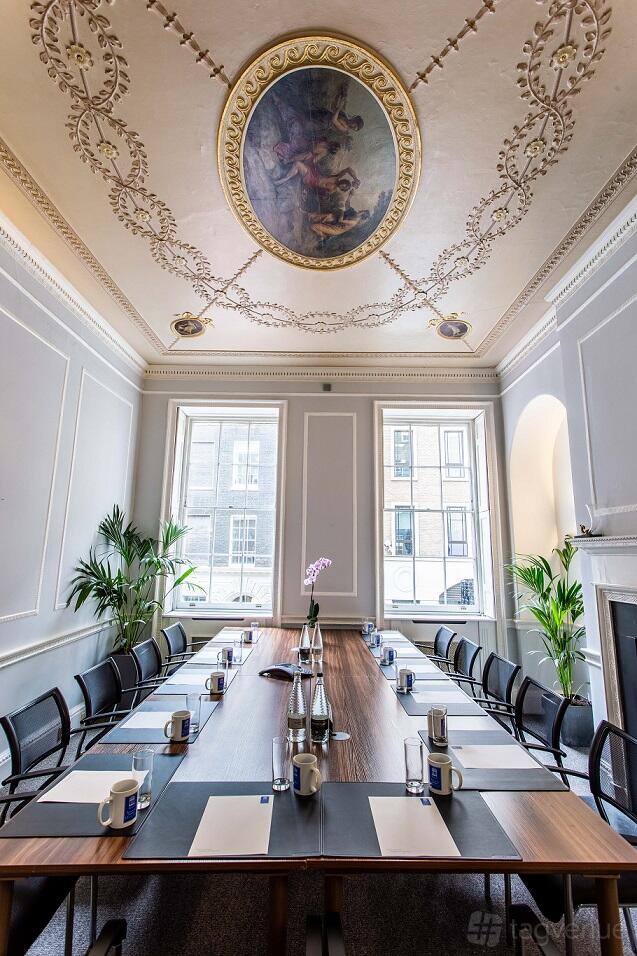 An event venue with ornate ceiling details, tall windows, and a long conference table at Adam House Event Space.