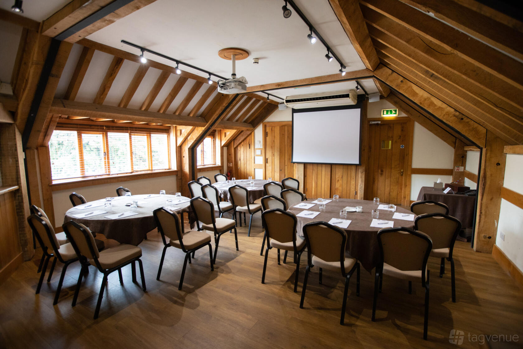A meeting room with exposed wooden beams, natural light from windows, and a projector screen at Tewinbury Farm Hotel.