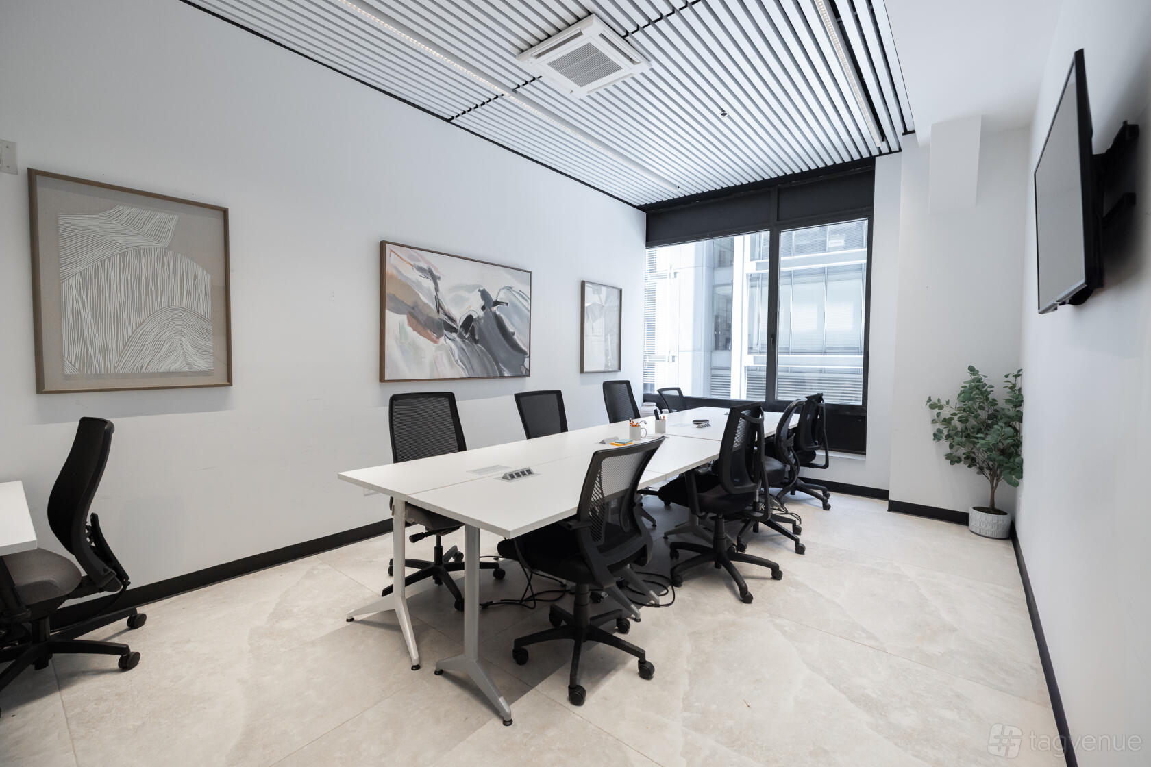 A boardroom with a long white table, black chairs, wall art, and large windows at Nomadworks - Times Square.