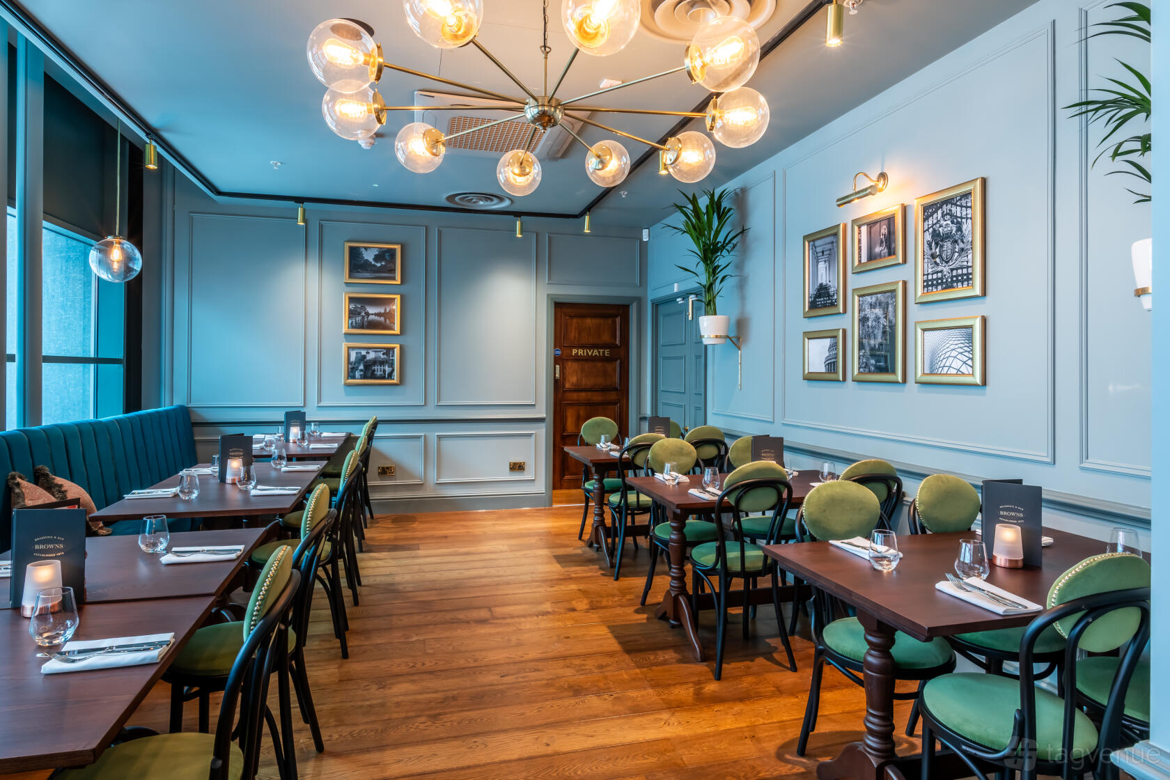 A dining room with wood floors, green chairs, globe chandelier, and framed photos on blue walls at Browns Victoria.