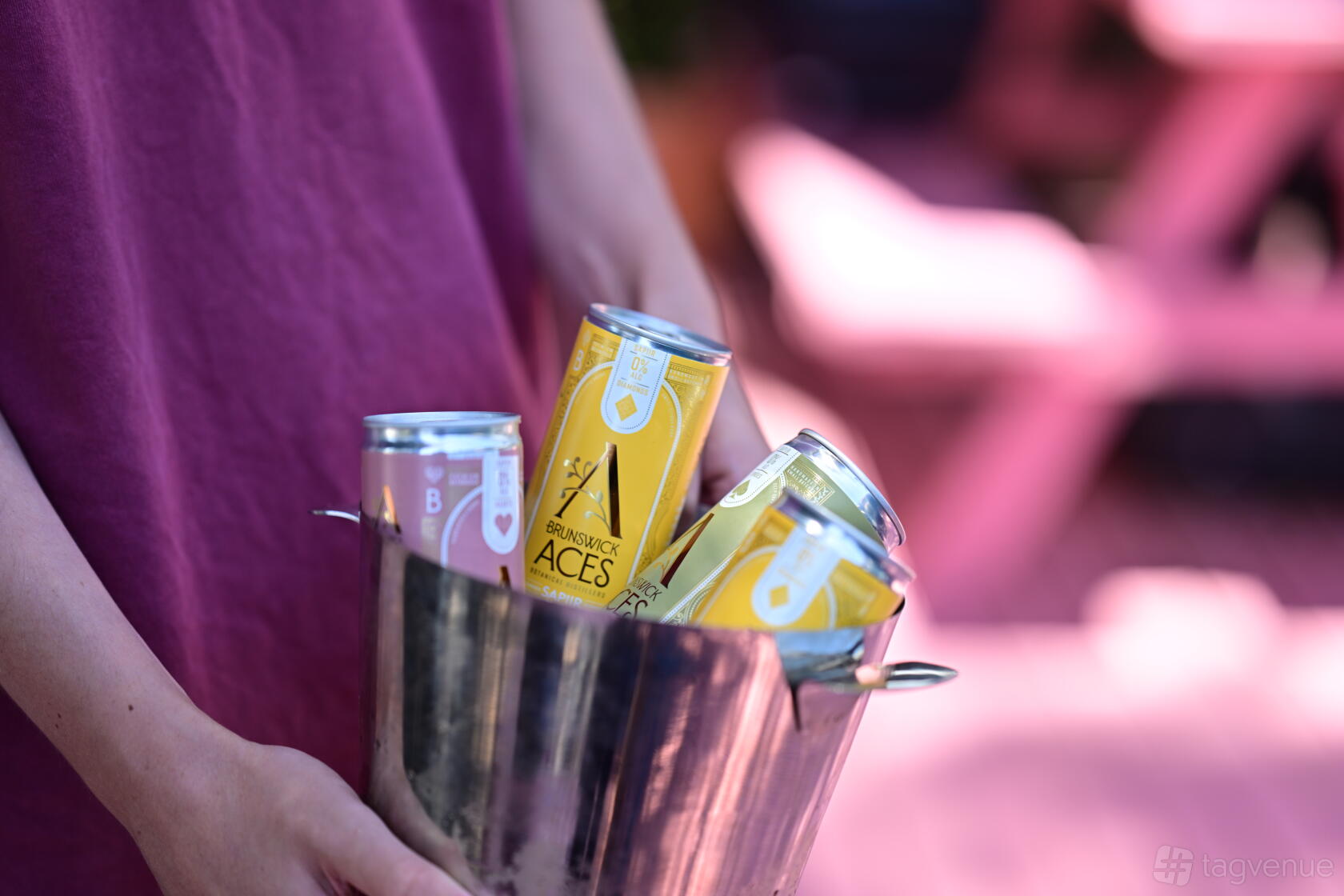 An outdoor bar scene with a person holding a metal bucket of Brunswick Aces canned drinks at Aces Bar.