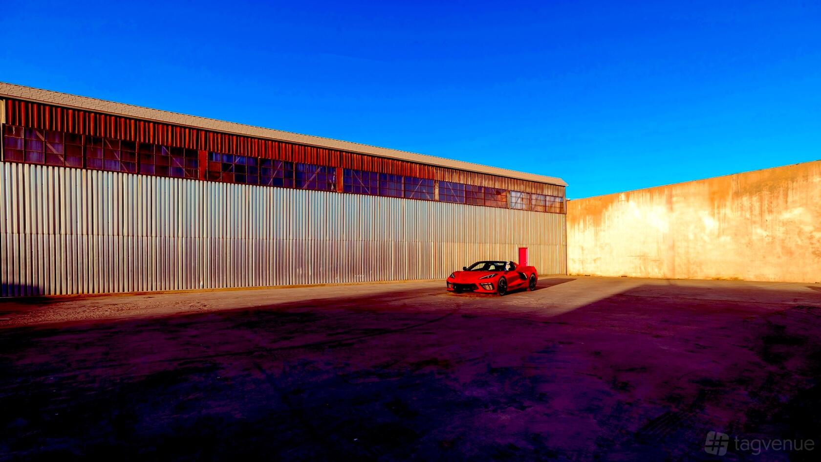 An outdoor creative space with corrugated metal siding, tall industrial windows, and a red sports car at Popsicle Studio LA.