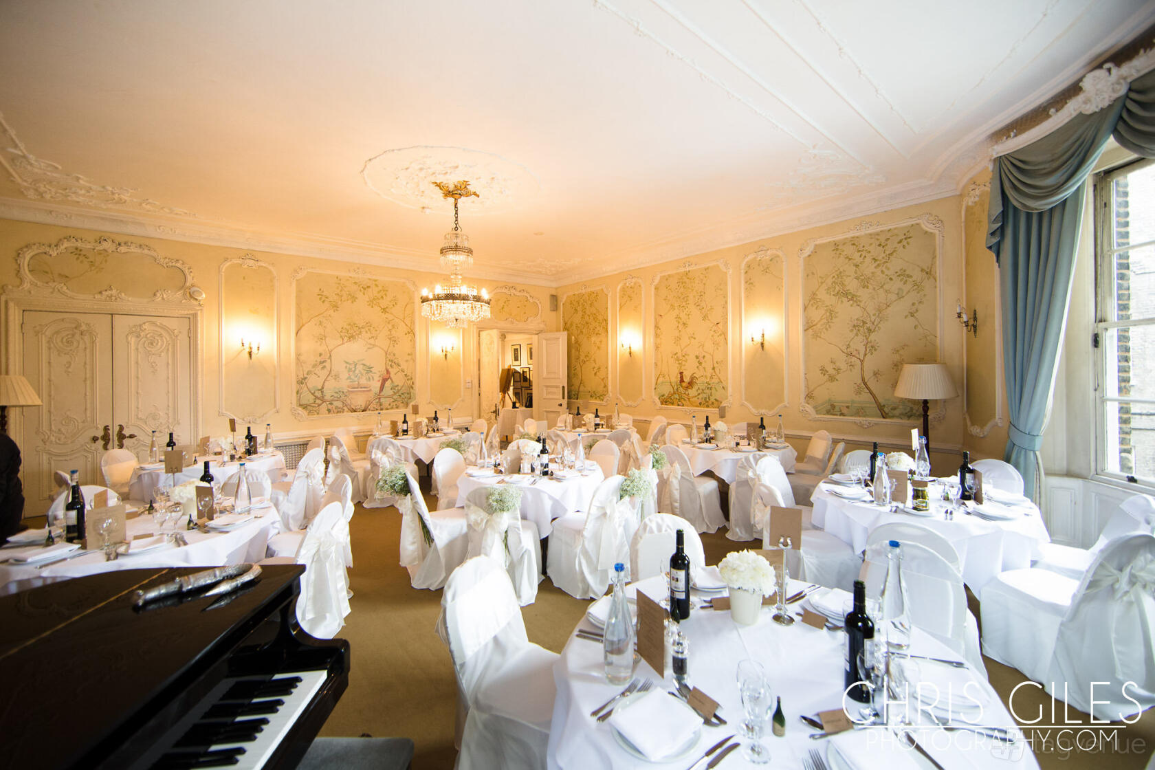 An event venue in a historic building with ornate wall moldings, chandeliers, and round tables set with white linens at University Women's Club.