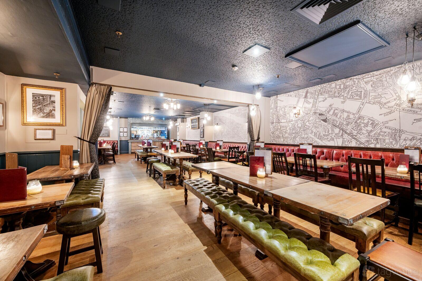 A function room in a pub with long wooden tables, red leather banquettes, and a map mural wall at The Horniman at Hays.