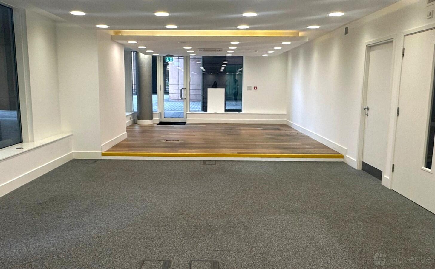 A creative space with white walls, recessed lighting, large windows, and a raised wooden platform at Elty Life Store.