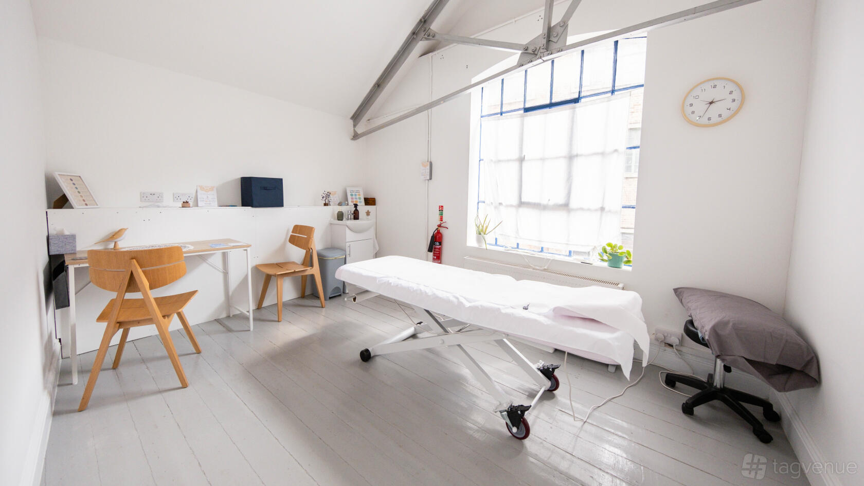 A therapy room with a treatment table, high ceilings, exposed beams, and large frosted windows at Prana Voice.