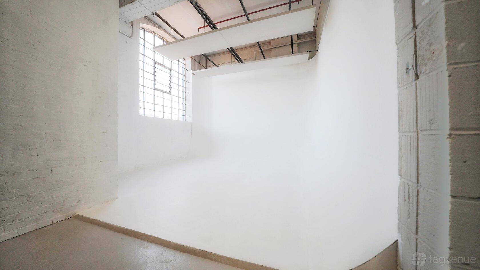 A photo studio with a white cyclorama wall, high ceiling, and large industrial windows at Stratford Workshops, Burford Road, E15 2SP.