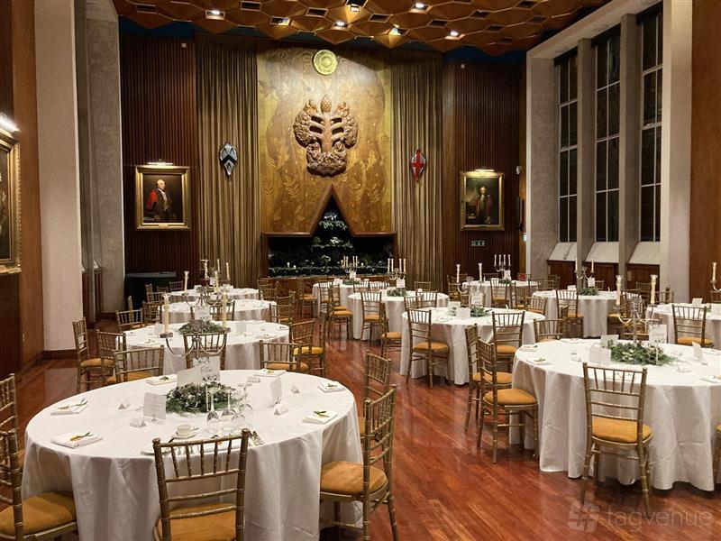 A formal hall with round tables dressed in white linens, gold chairs, and wood floors at Carpenters' Hall.