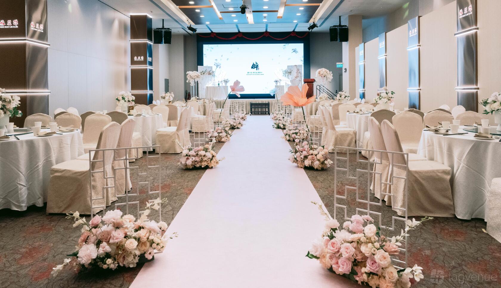 A banquet hall with a white aisle runner, floral arrangements, and round tables with white chairs at Chui Huay Lim Teochew Cuisine.