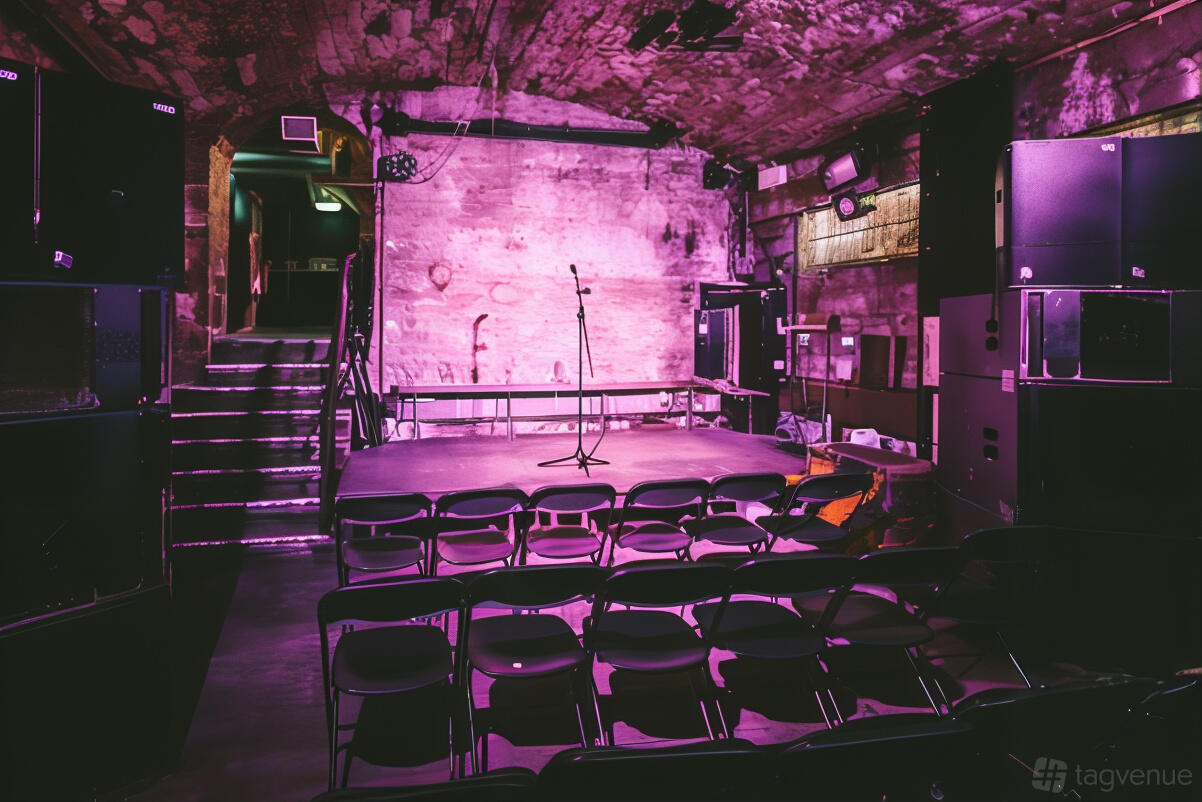 A nightclub with a small stage, microphone, folding chairs, and arched stone walls at The Cabaret Voltaire.