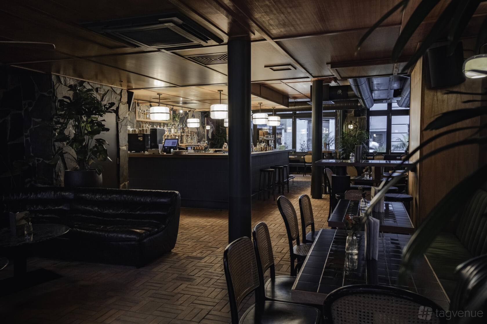 A bar with wood-paneled ceilings, black leather seating, and indoor plants at Two Floors.