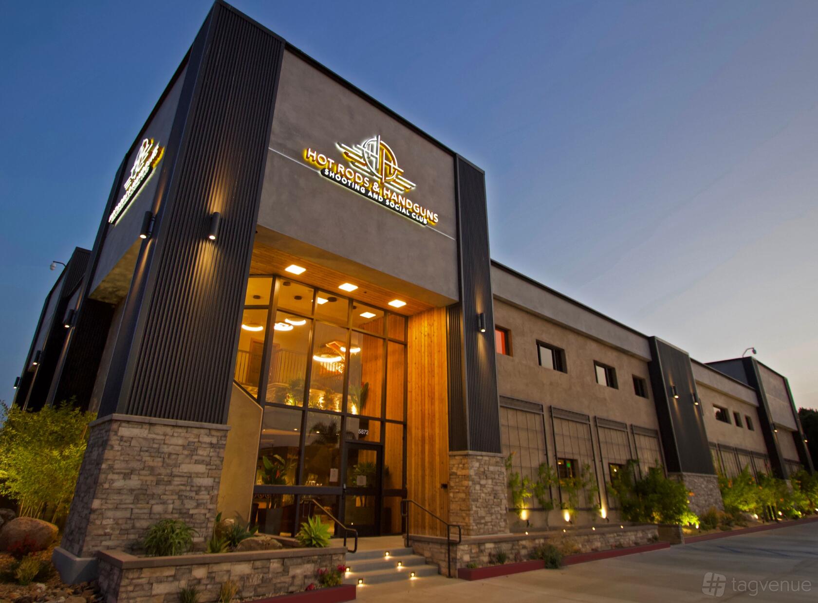 A versatile event space with modern architectural facade, large windows, and illuminated signage at Hot Rods & Handguns.
