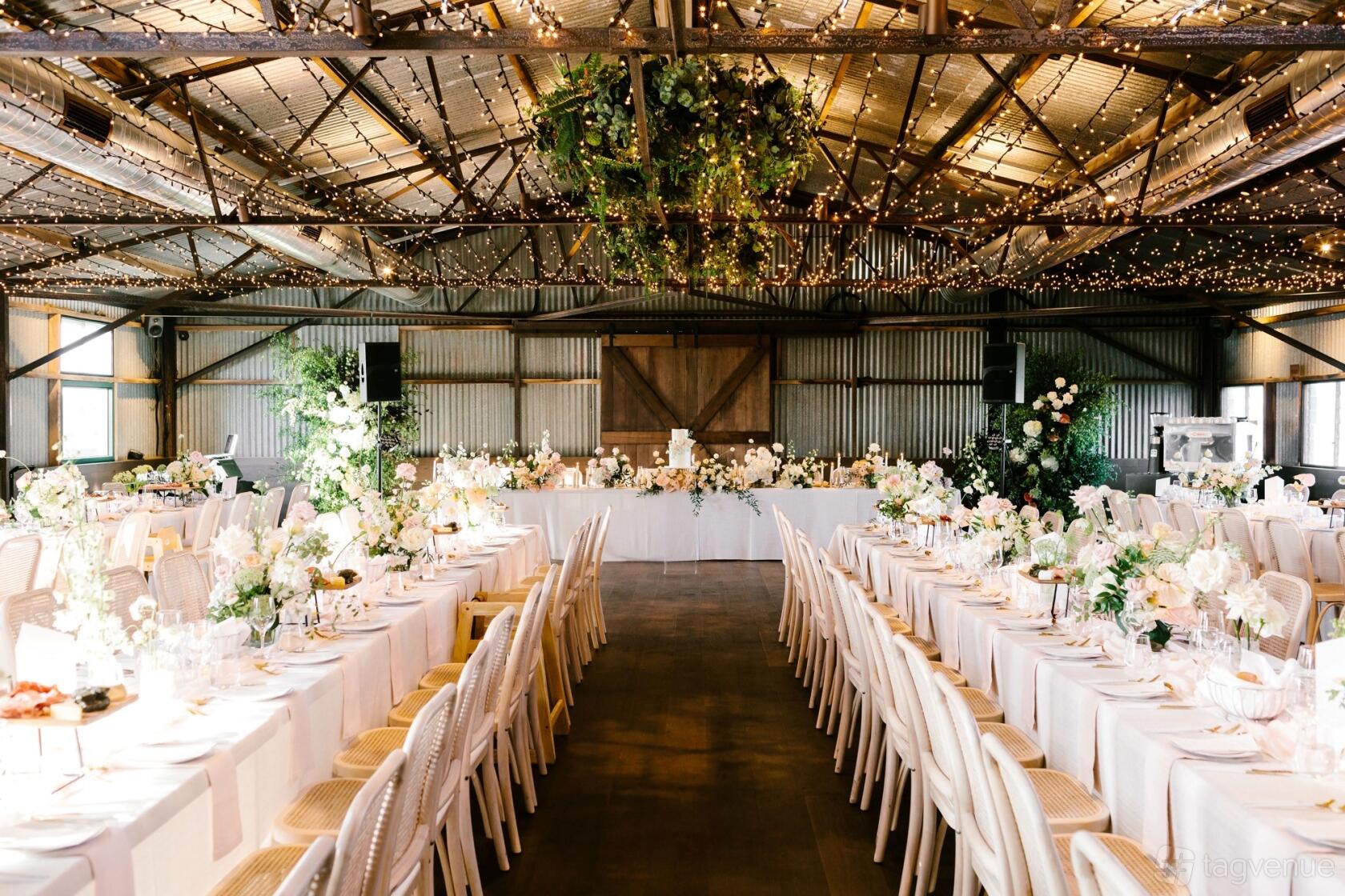 An event space in a winery with long banquet tables, white chairs, and hanging greenery at Marnong Estate The Woolshed.
