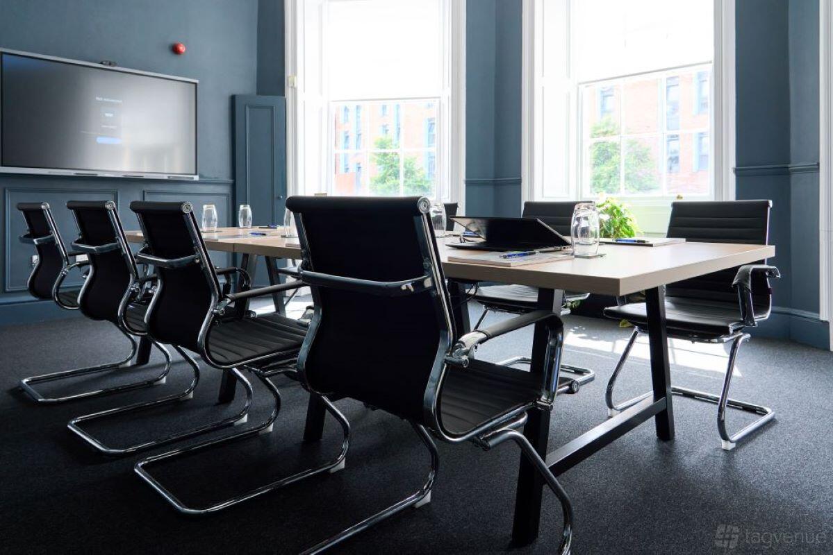 A boardroom with black executive chairs, a rectangular table, and tall sash windows at Clavering House.