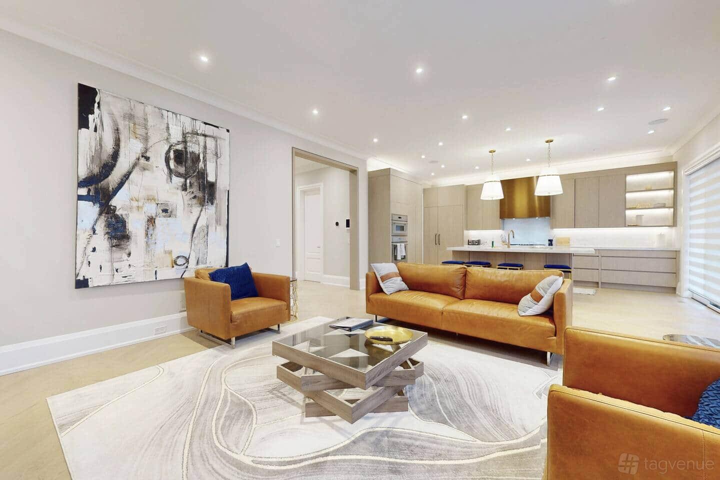 A living area with tan leather sofas, abstract wall art, and an open kitchen with pendant lighting at Luxury Designer Home in Etobicoke.
