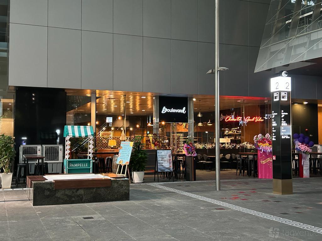 An outdoor area with cafe tables, decorative signage, and a striped booth at Boulevard at Asia Square.