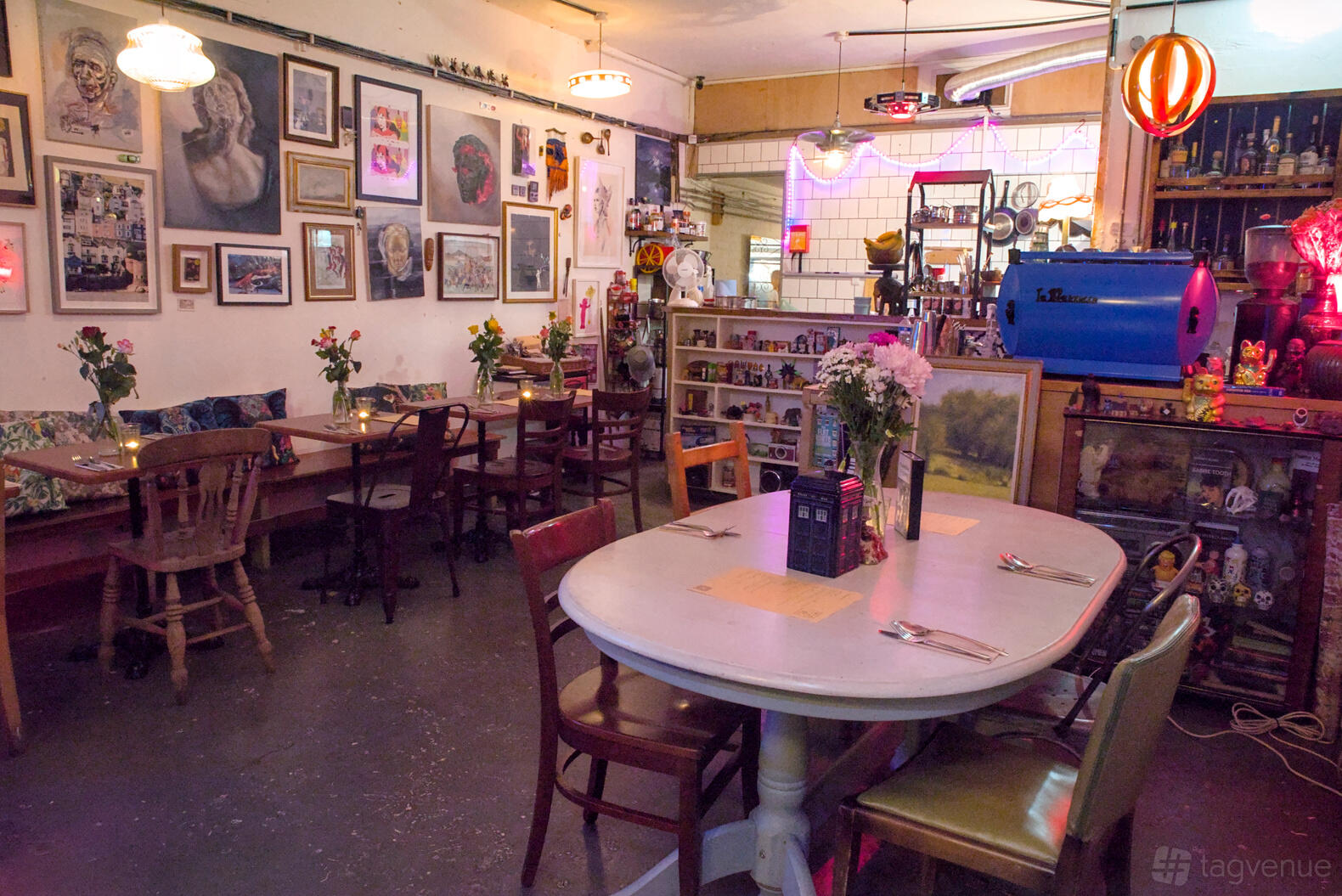 A restaurant with eclectic wall art, mismatched chairs, and floral centerpieces on wooden tables at Sabretooth.