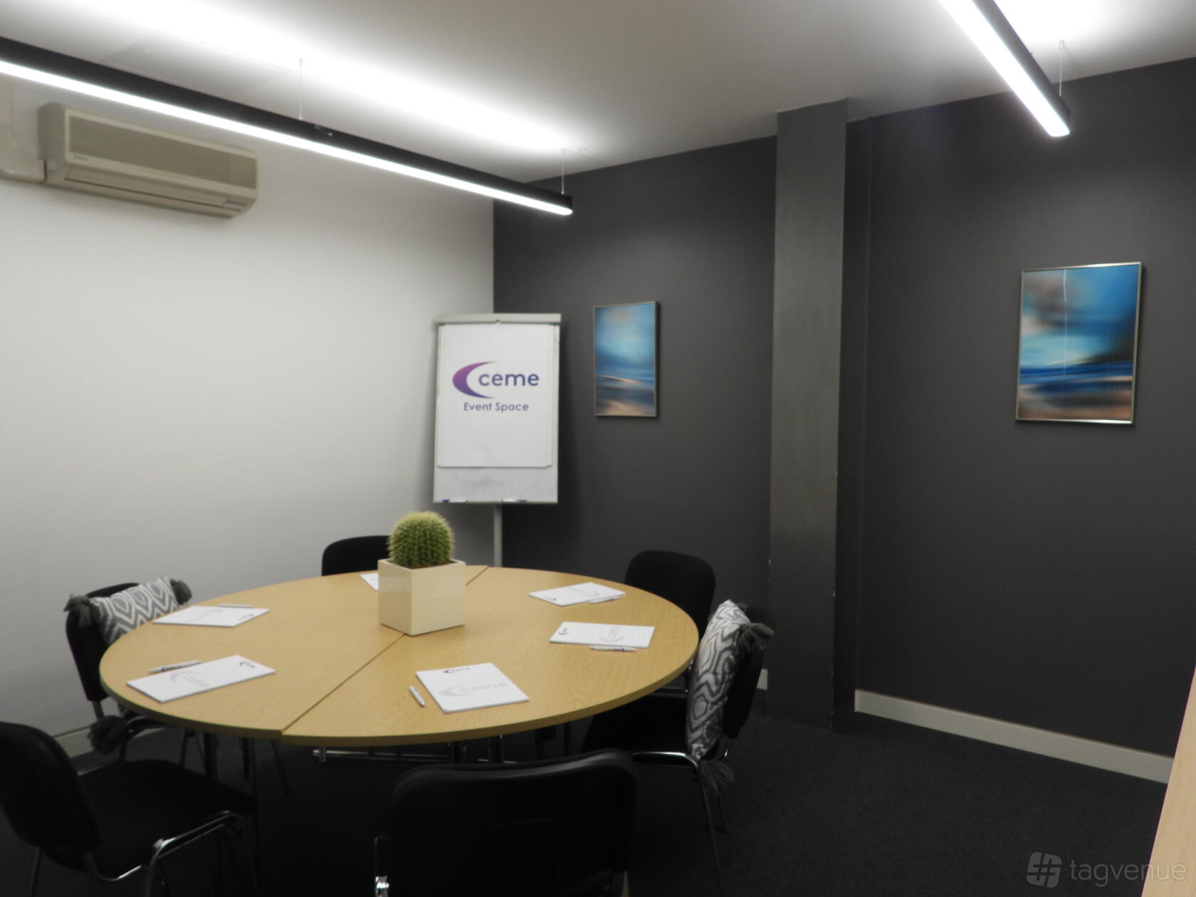 A meeting room with a round table, six chairs, a flipchart, and wall art at Event Space CEME.